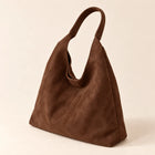 Coffee faux suede shoulder bag in a rear three-quarter view on sand