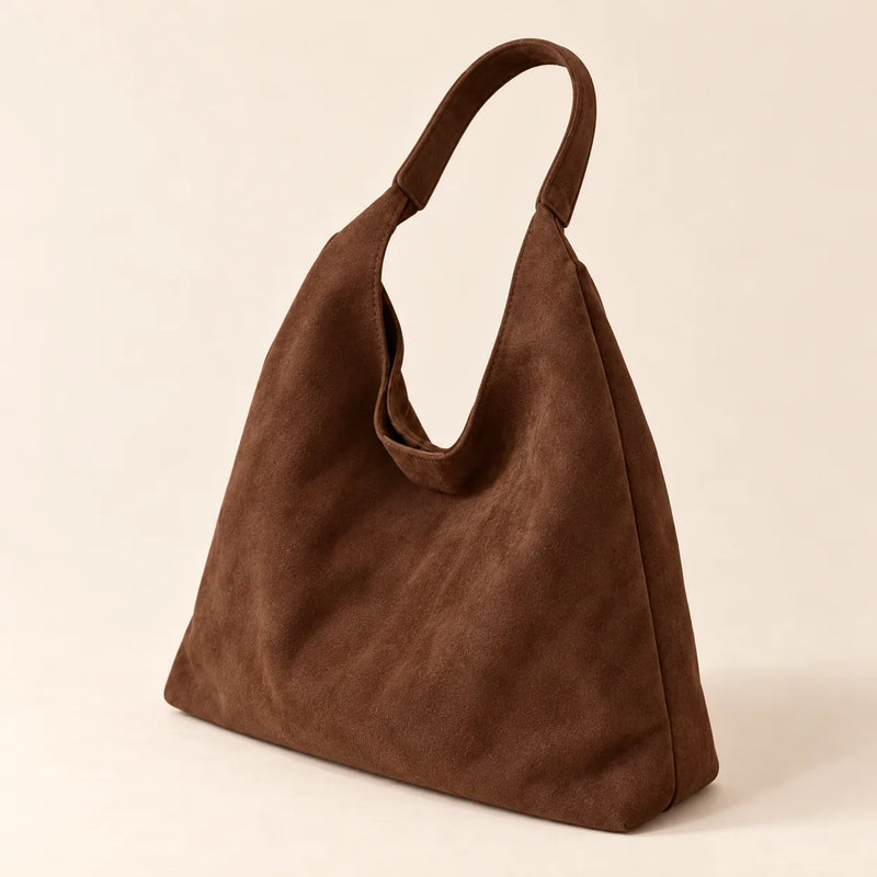 Coffee faux suede shoulder bag in a rear three-quarter view on sand