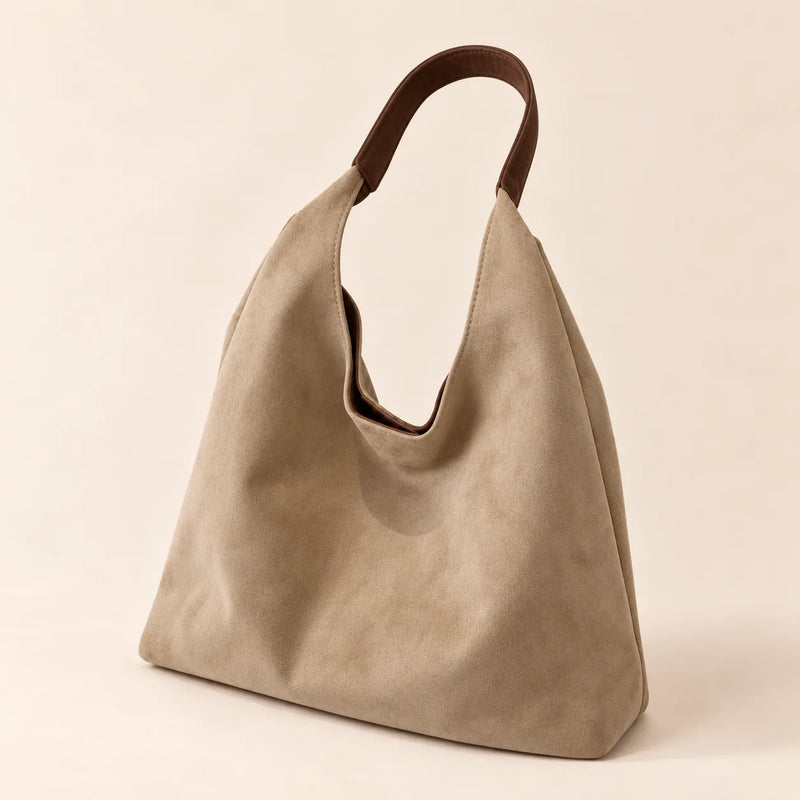 Beige faux suede shoulder bag with a single fixed strap on a sand background