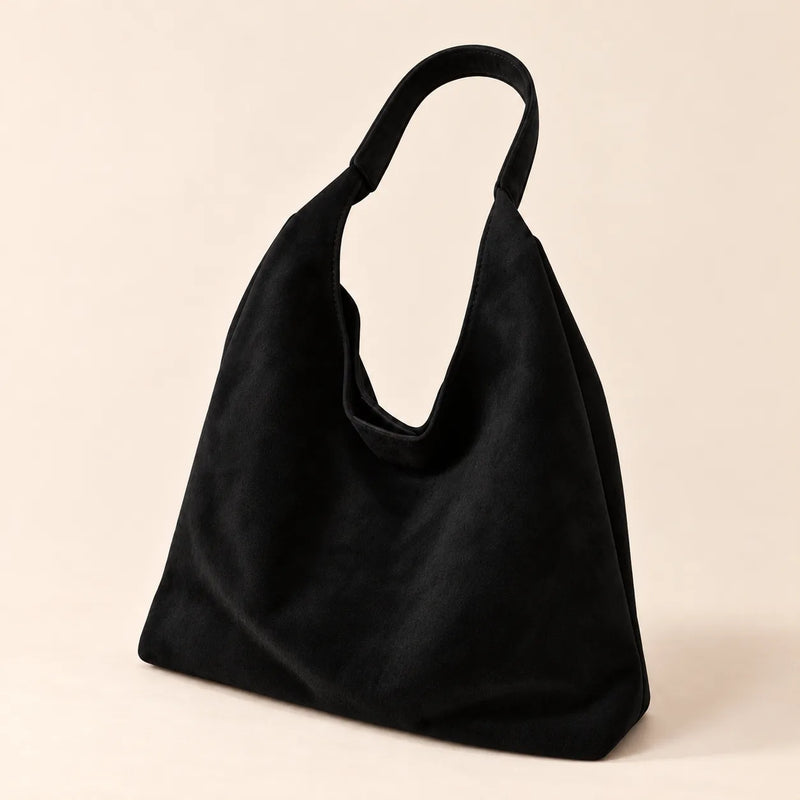 Black faux suede shoulder bag with a single fixed strap on a sand background